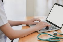 Image du médecin en train de travailler sur son ordinateur portable avec son stéthoscope posé à côté